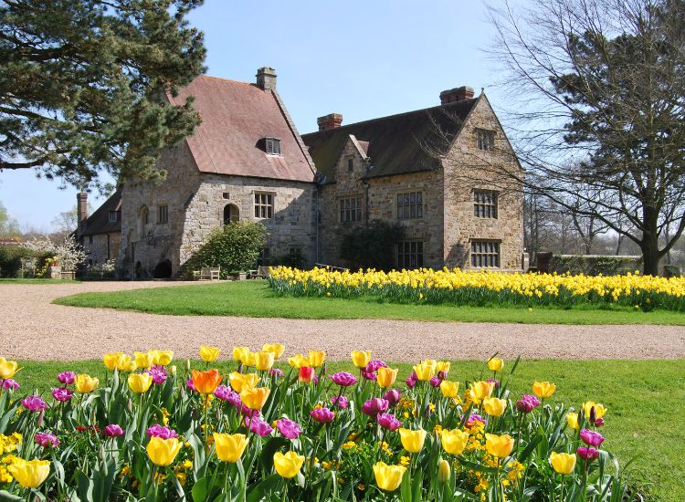 A medieval priory building with tulips surrounding the exterior